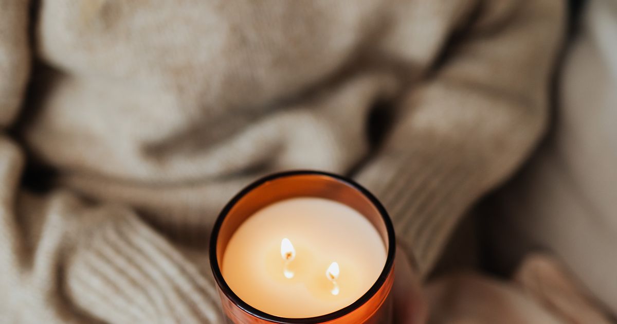 Nő meleg itallal és égő gyertyával egy otthonos, csendes esti pillanatban