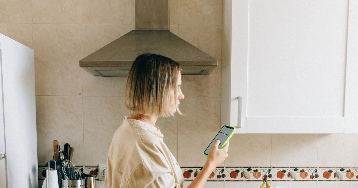 Kimerült dolgozó anya a konyhában telefonon tradwife-tartalmat néz
